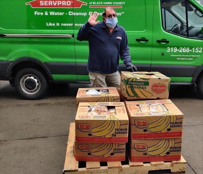 A jolly man waving and standing in front of a pallet of boxed food.