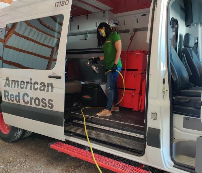 American Red Cross Transit with their side door open and a woman spraying a white mist in the truck.