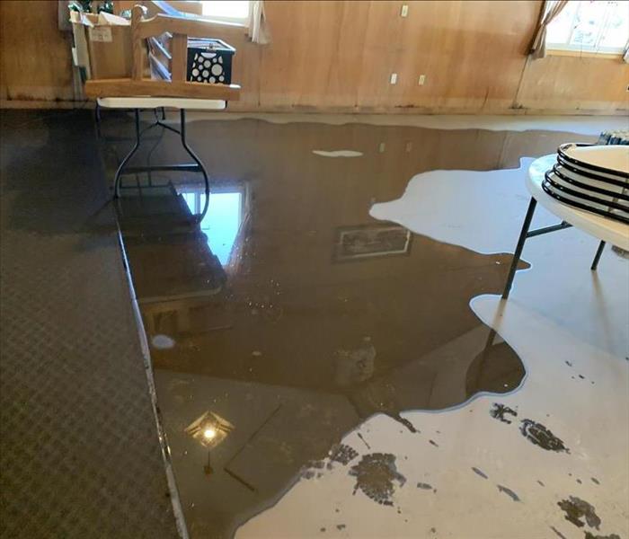 Puddle of water covering cement flooring and carpets in a large hall with tables.
